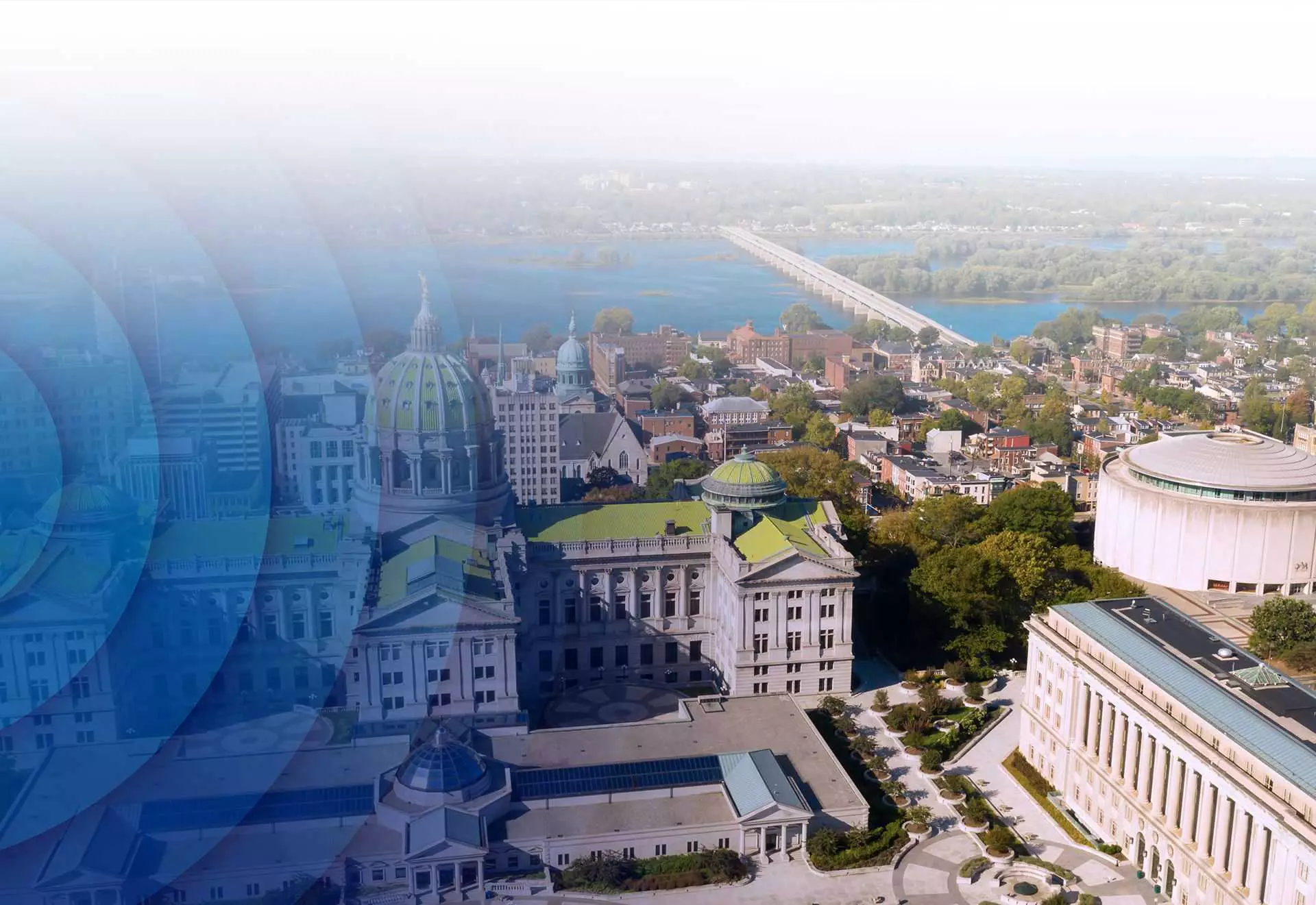 Aerial view of a domed government building complex and surrounding cityscape near a river with a bridge in the background.