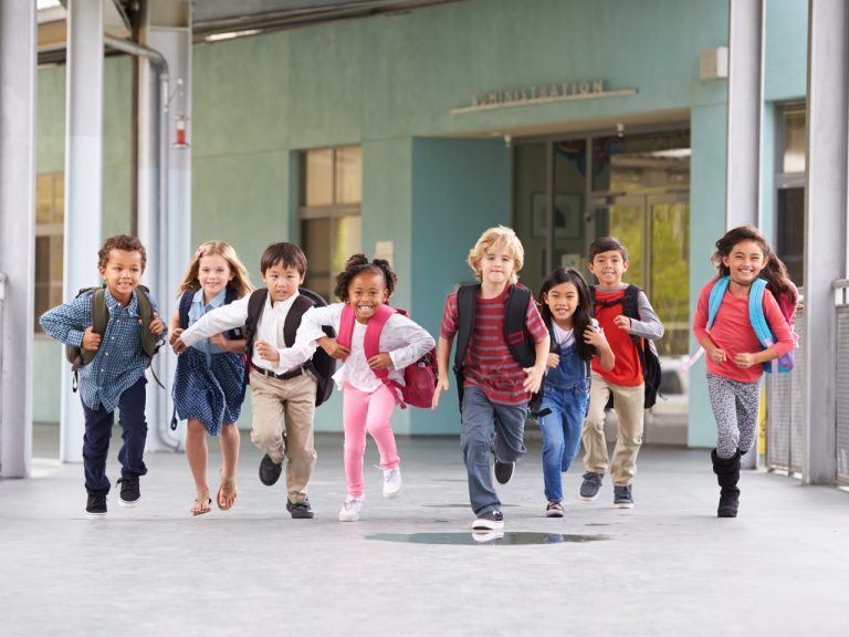 A group of elementary school children running together in a school corridor.
