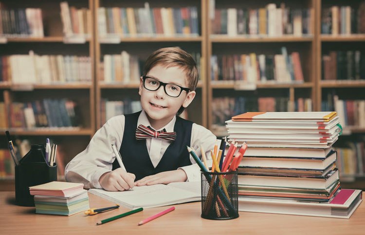 A young student dressed in a vest and bowtie studying in a library.
